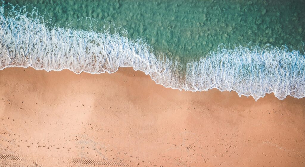 Aerial view of gentle waves meeting sandy beach on a sunny day, perfect for relaxation.